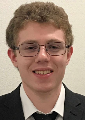 Ben is a white male with brown hair and glasses, smiling, and wearing a black suit, white shirt, and black tie with small white dots.