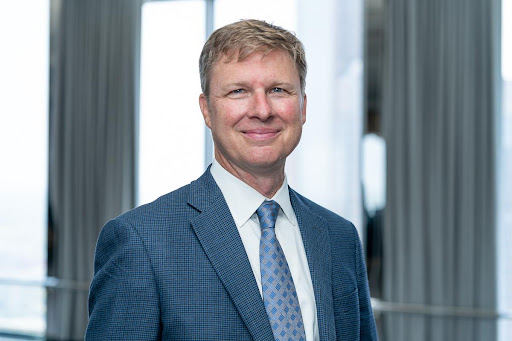 Headshot of Derek Shields, a white male smiling with blonde hair wearing a blue suit and tie.