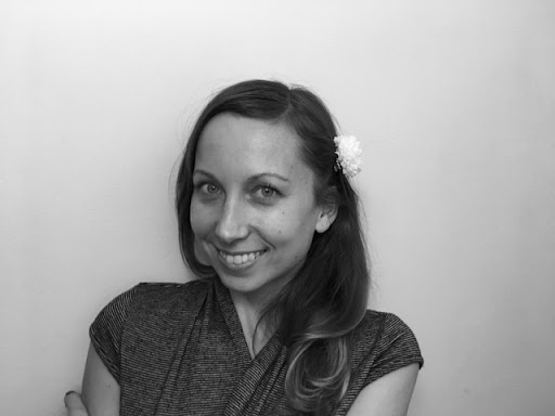 Black and white photo of Emma. She wears a short sleeved shirt and has long hair, pulled back on the side with a flower.