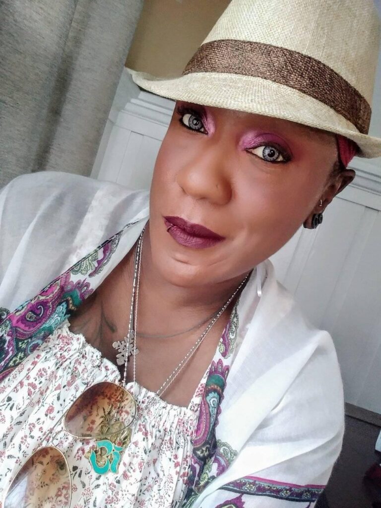 Trelanda-Lowe African American woman with a beige fedora and white outfit with Paisley pattern along the edges.